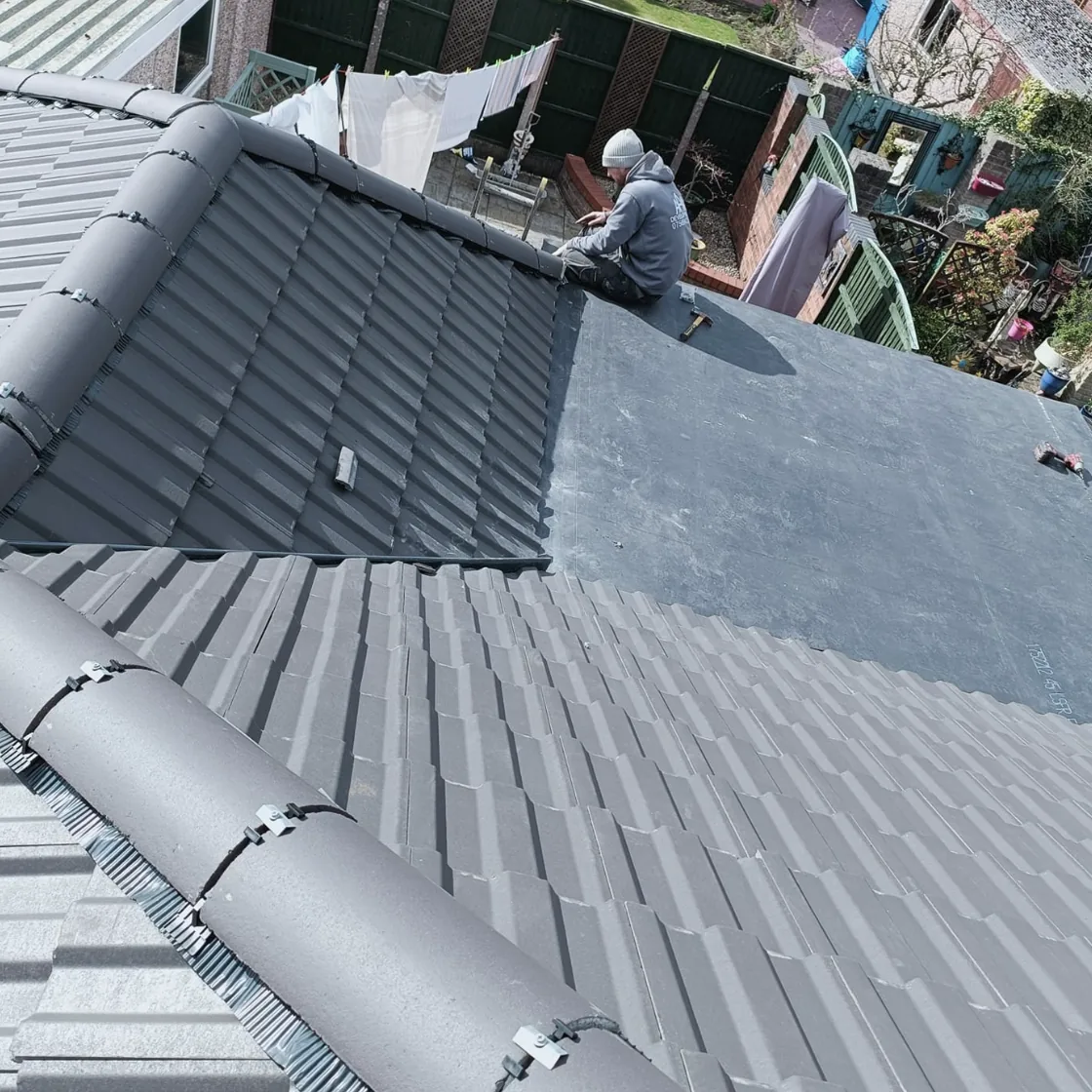 Roofer working where a flat roof meets pitched tiles