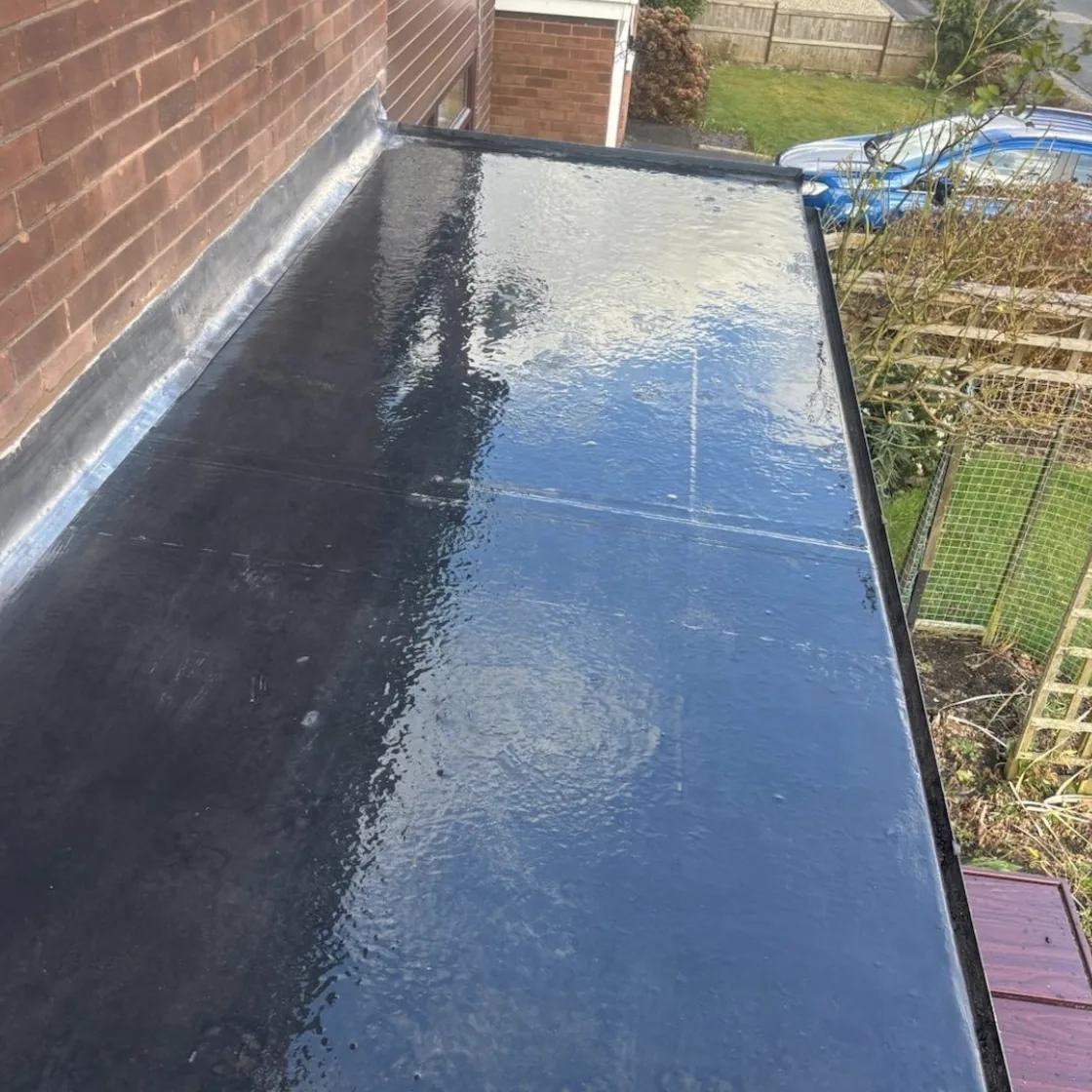 Dark flat roof surface beside a brick wall