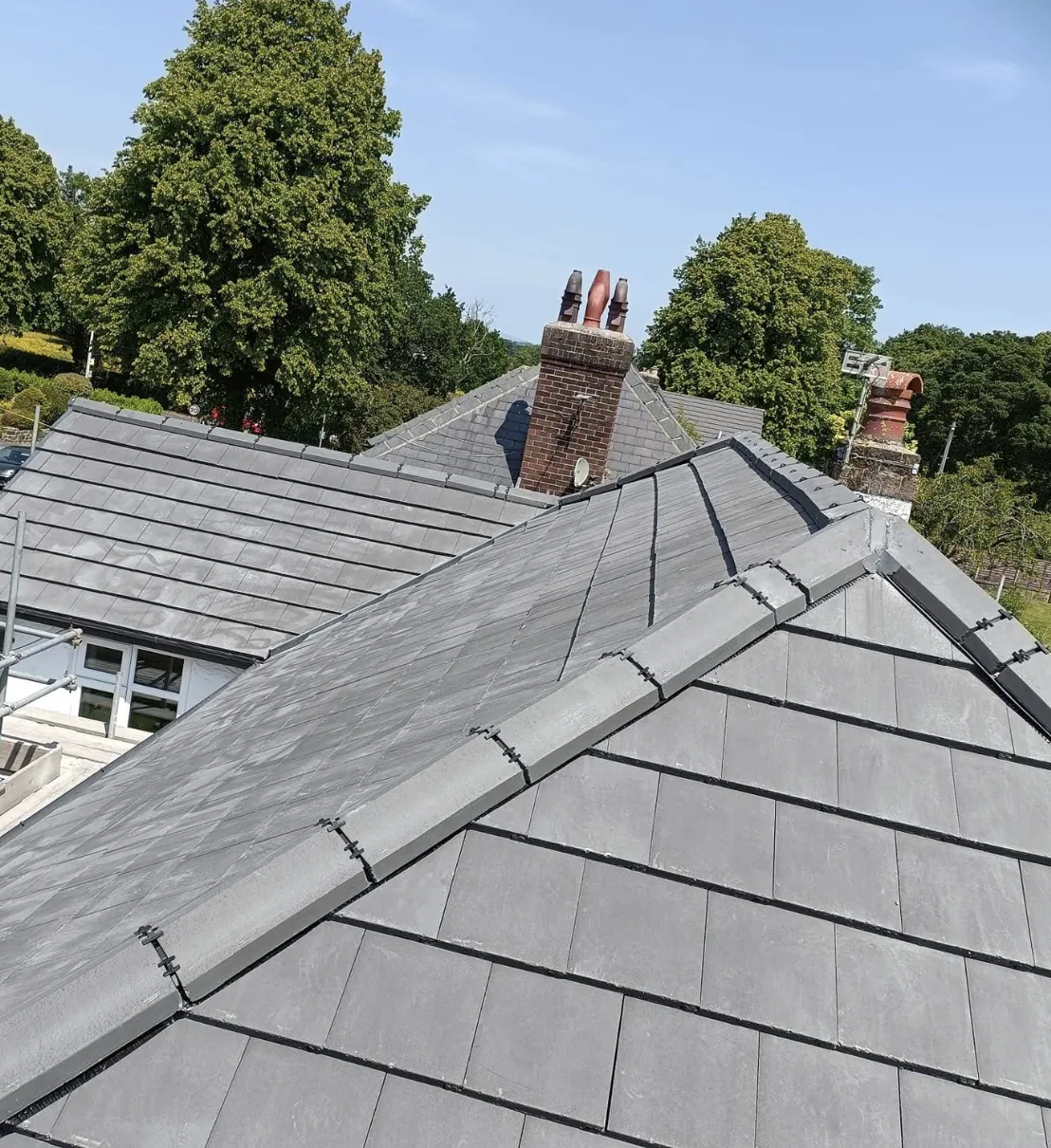 Grey tiled roof hips with chimneys behind