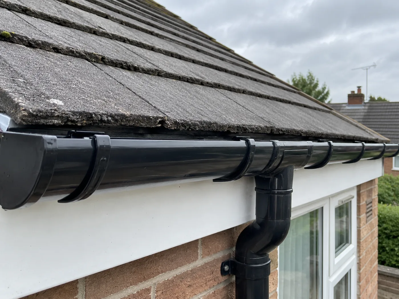 Black guttering and downpipe fitted along a tiled roof edge